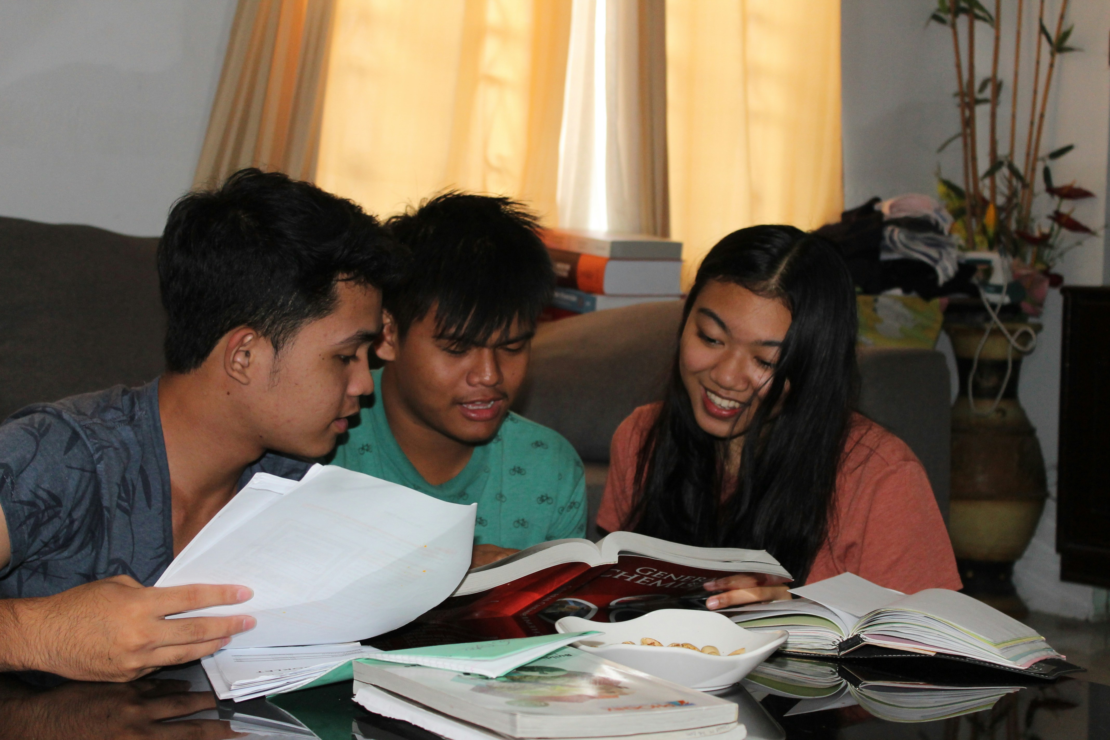 A girl and two boys sitting together and studying surrounded by school books.