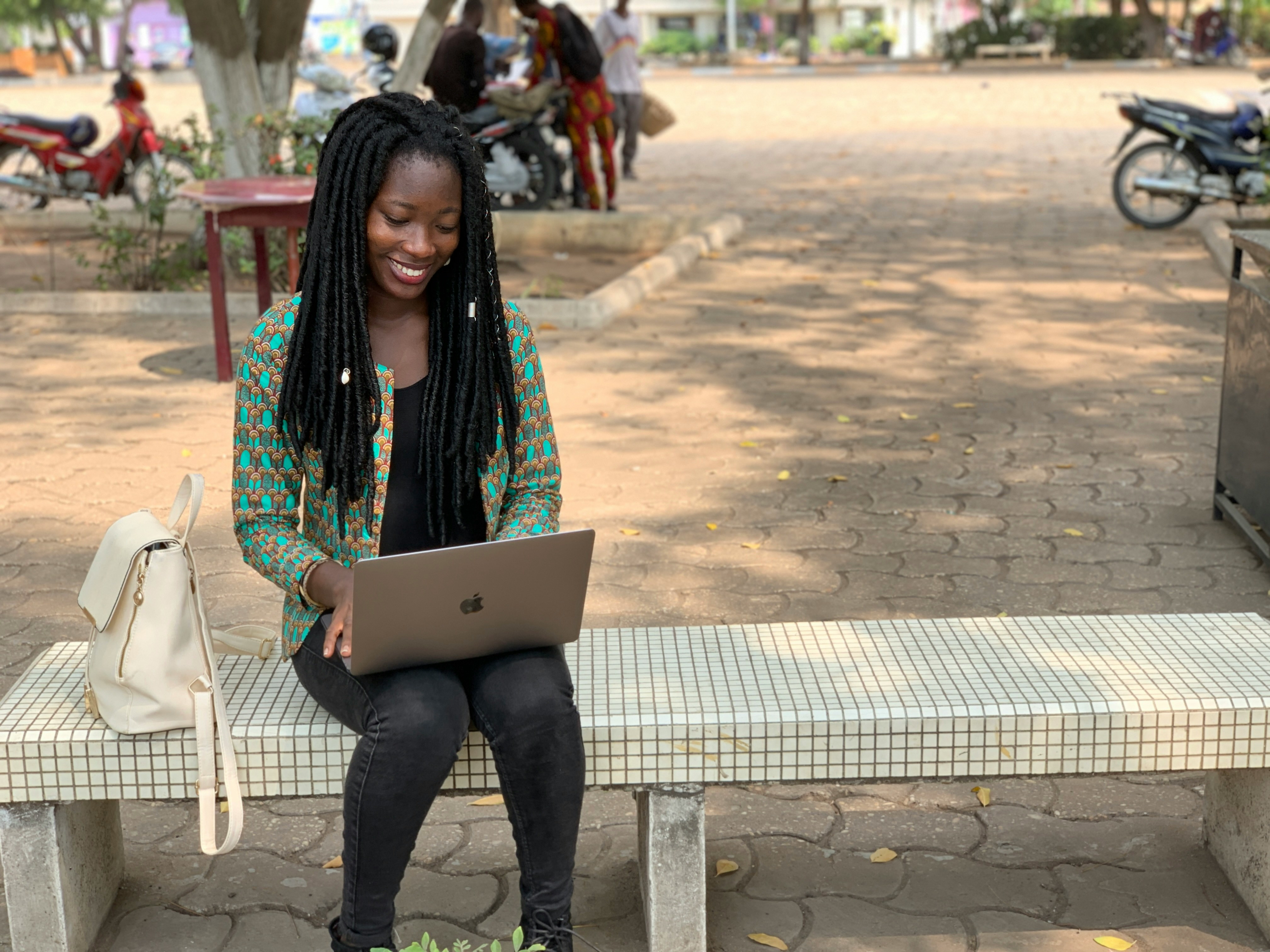 A girl sitting on a bench looking at her laptop in a hopeful expression.