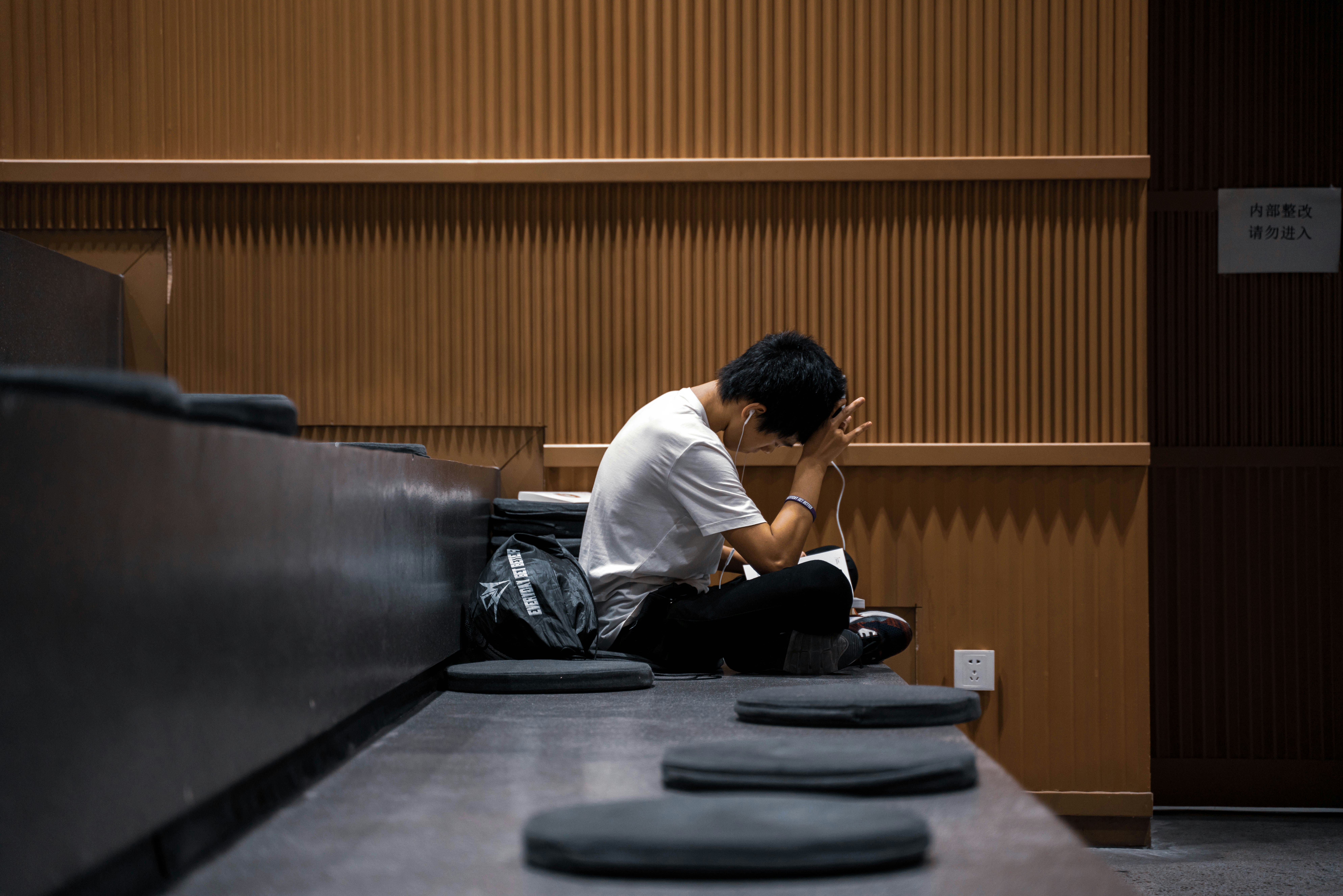 A student in white shirt sitting on the stairs studying with an uncertain expression with a hand on his head.